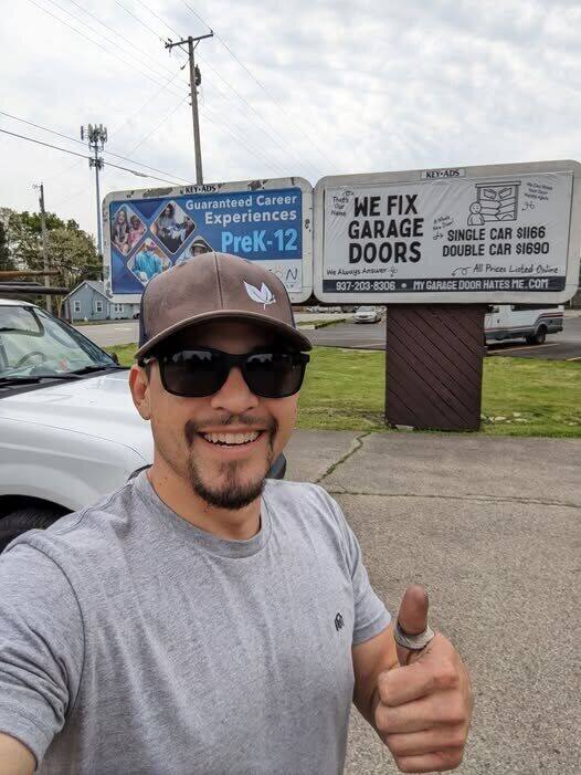 We Fix Garage Doors owner in Dayton, prices posted on the billboard behind him