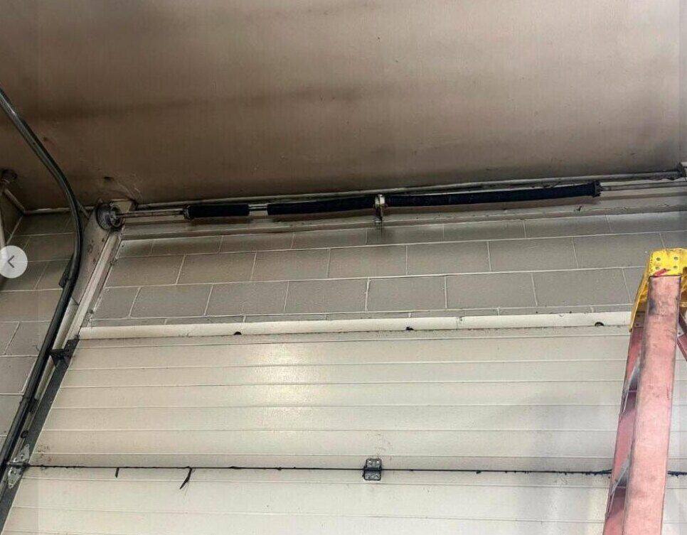 Technician replacing a garage door spring on a ladder